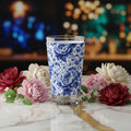 A clear drinking glass featuring a blue and white floral peony pattern, shown on a solid white background.