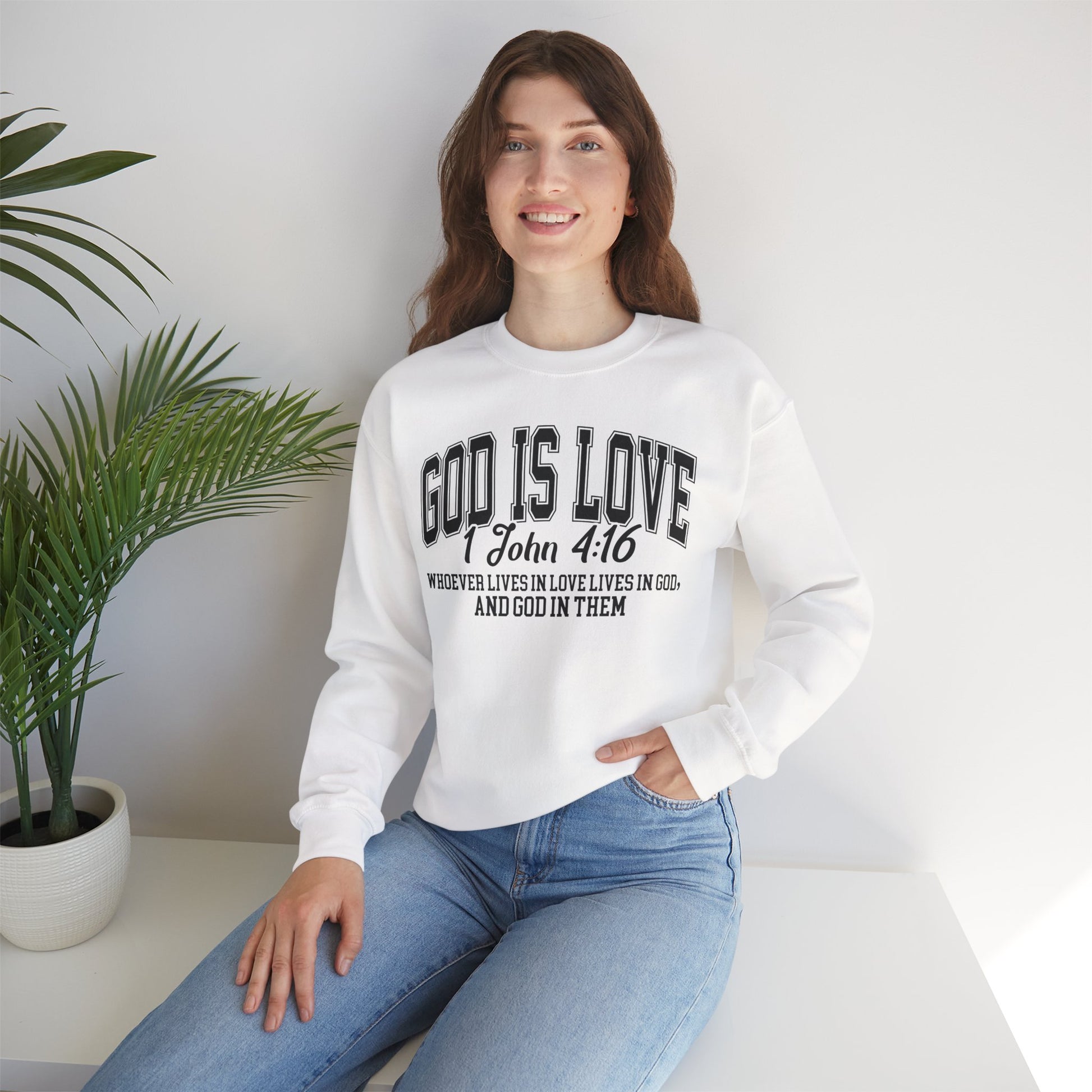 Woman wearing a white sweatshirt with 'GOD IS LOVE' text, sitting in a room with a plant.