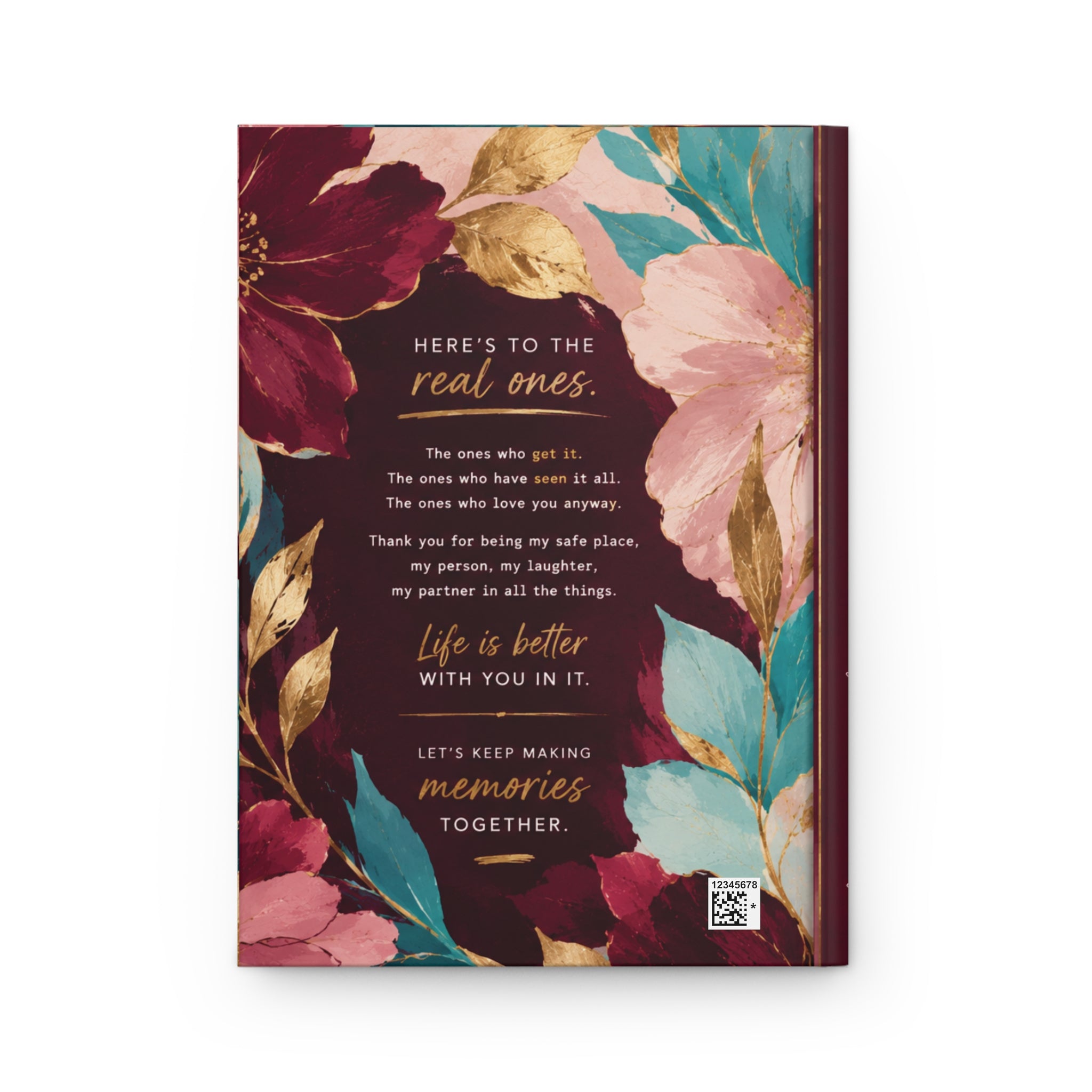A hardcover journal with a floral cover design, featuring dark red, pink, teal, and gold watercolor flowers with a central quote printed in white and gold text.