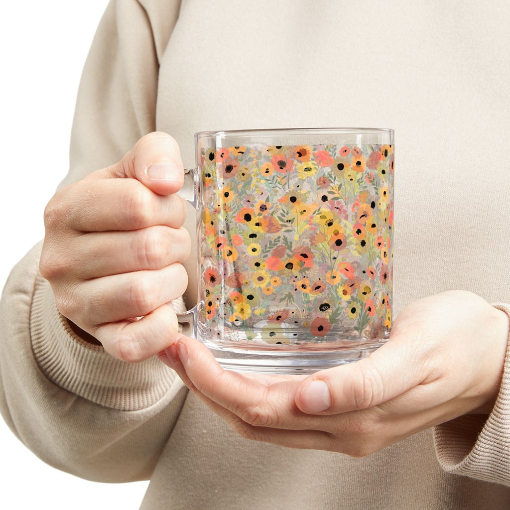 Person holding a clear mug with colorful floral pattern against a plain background