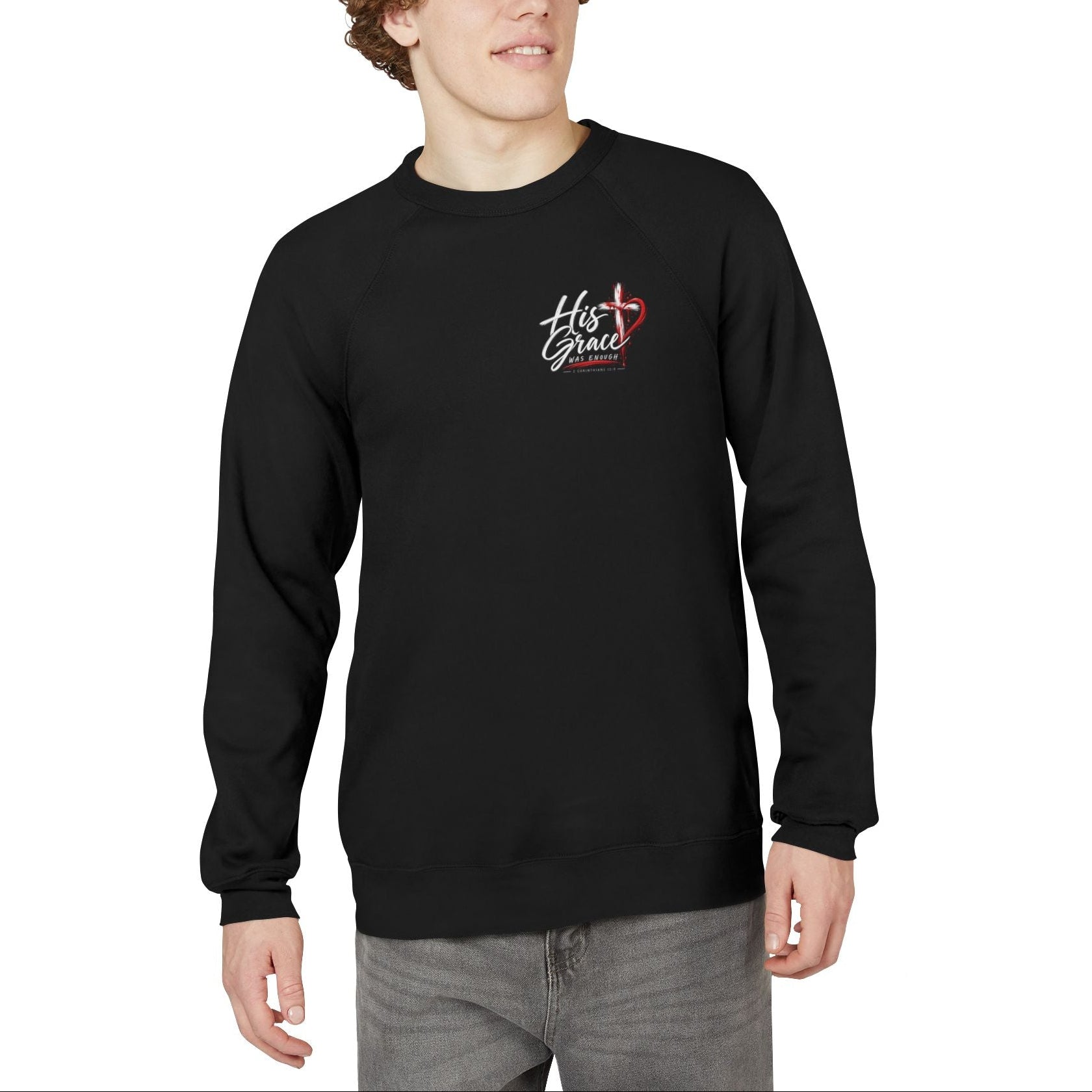 A man with curly brown hair wearing a black crewneck sweatshirt with a small white and gold crest on the left chest, paired with gray jeans, against a plain white background.