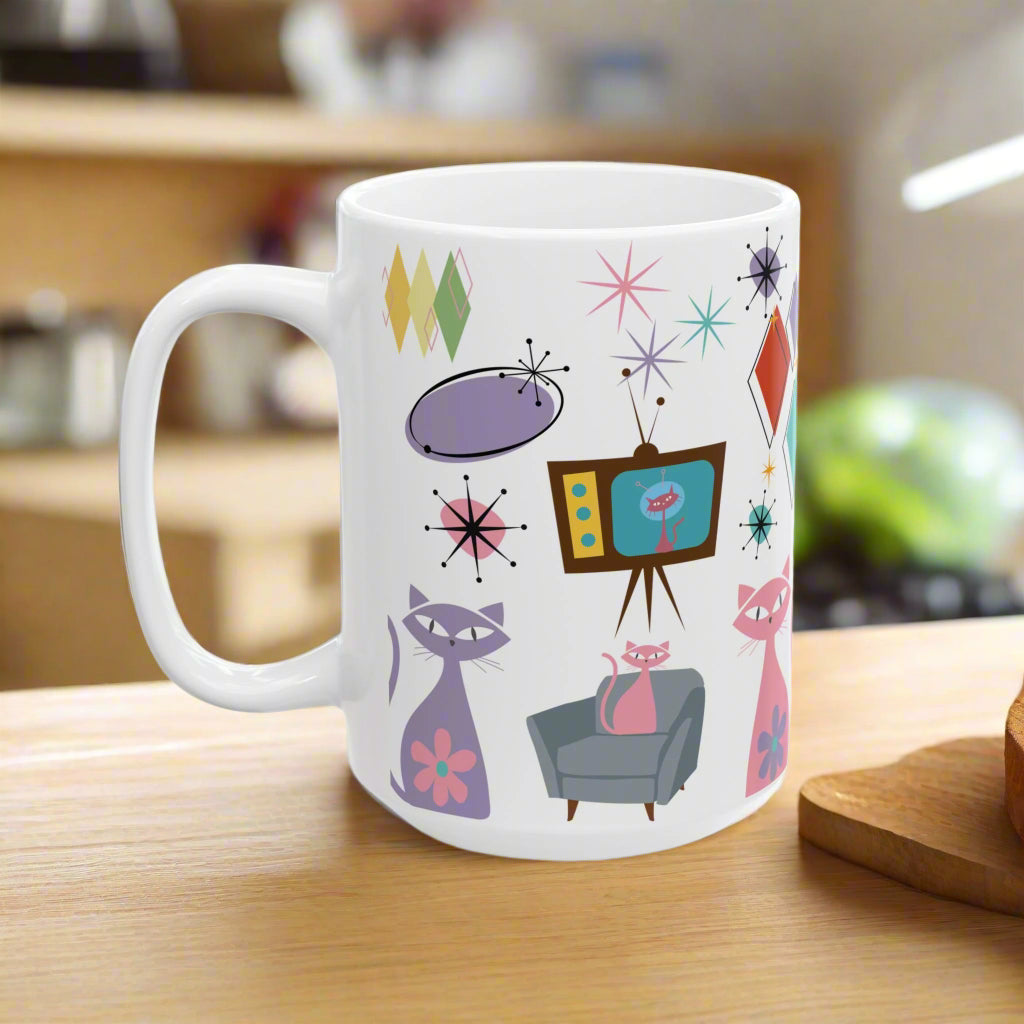 White mug with mid-century modern design featuring cats, a TV, and abstract shapes on a white background.