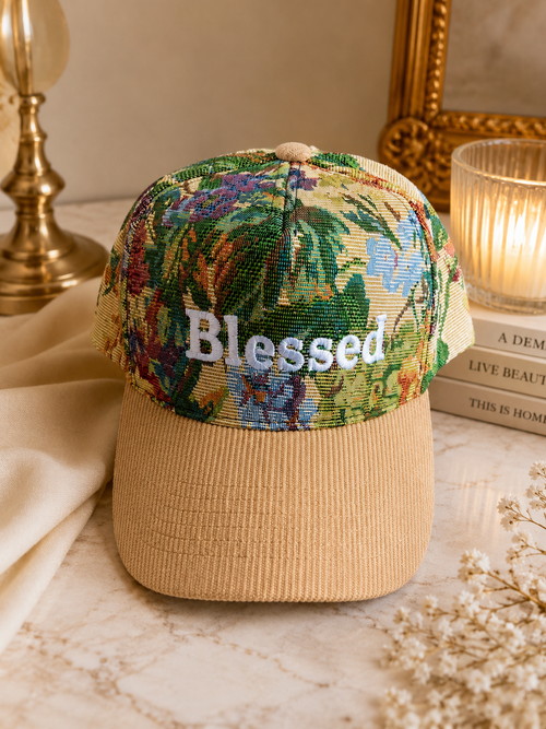 Beige cap with floral brim and 'Blessed' text on a decorative surface.
